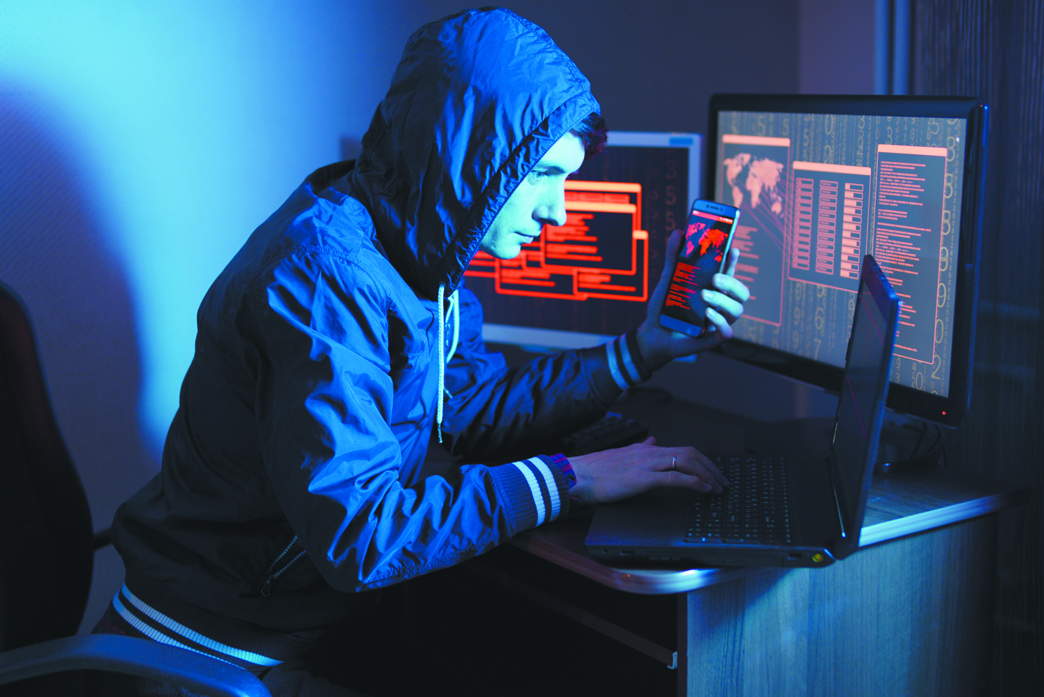 Hacker in the hood holding the phone in his hands trying to hack the mobile device cloud in neon light. Cyber security