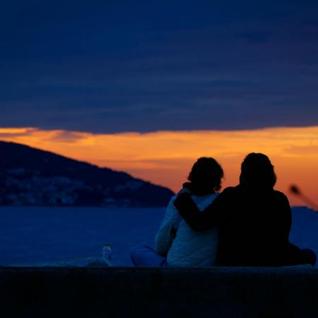 couple sitting on sea shore at sunset