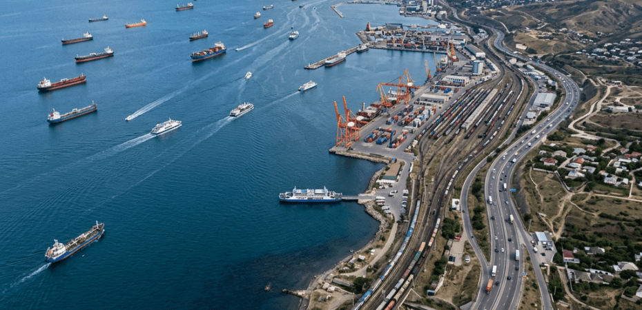 Aerial view of a coastal port with ships, cranes, railways, and highways